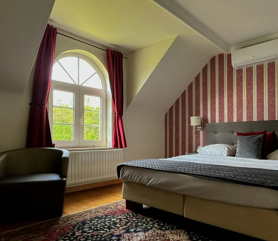 Hotelkamer met boogvenster, rode gordijnen en een tweepersoonsbed